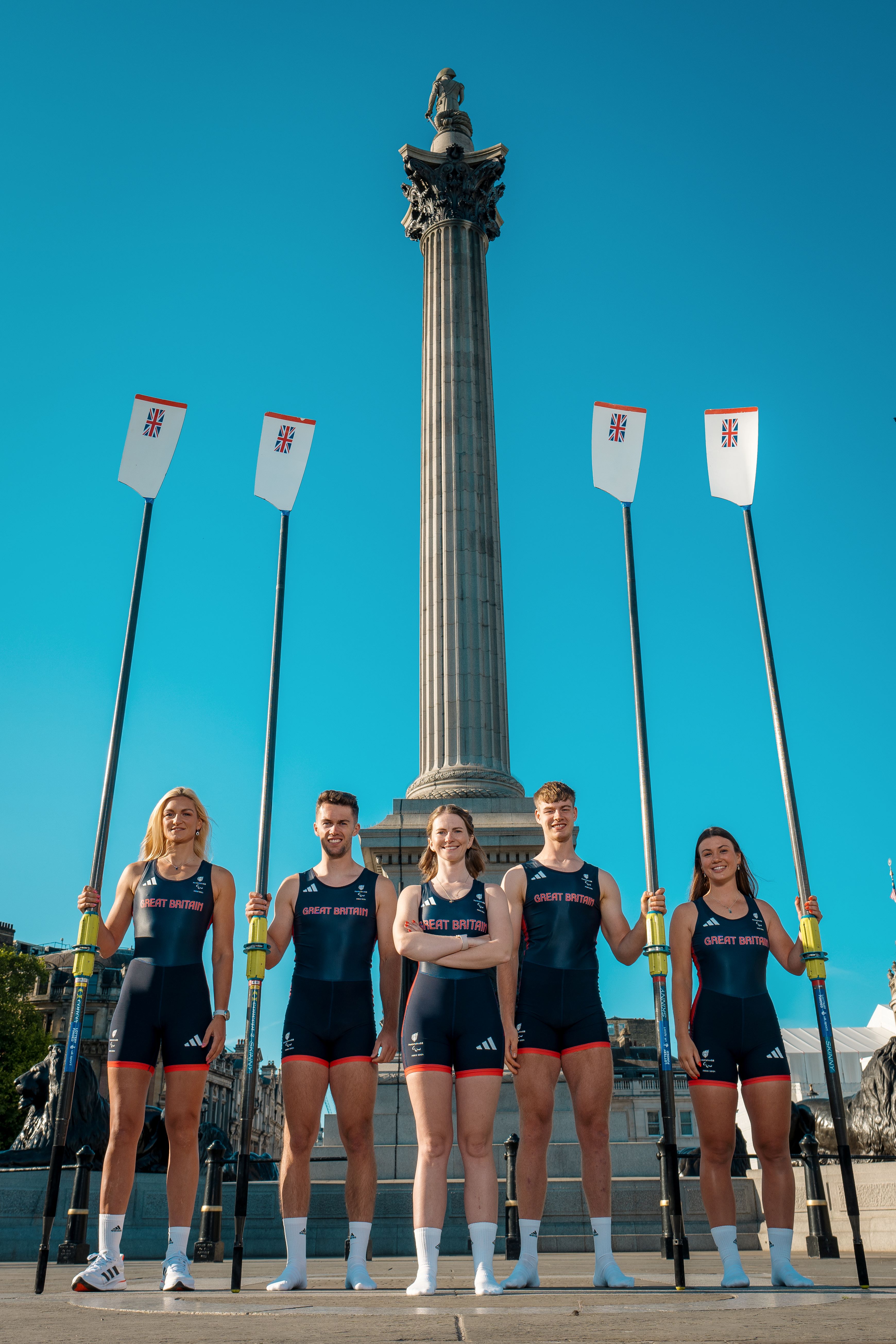 Erin (centre) and her teammates pose in front of a monument, holding four oars.