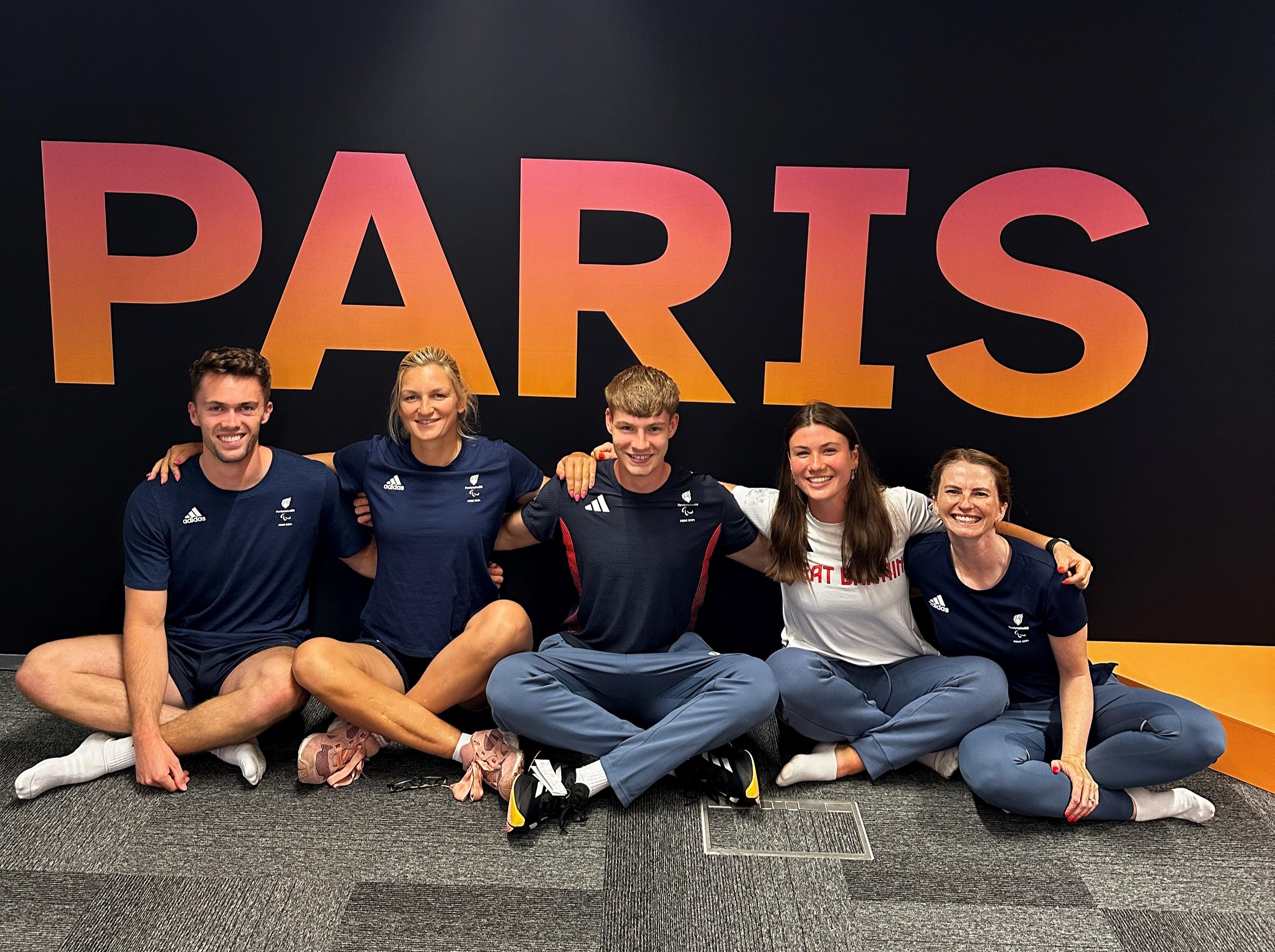 Erin and team members pose seated in front of a sign saying 'Paris'.